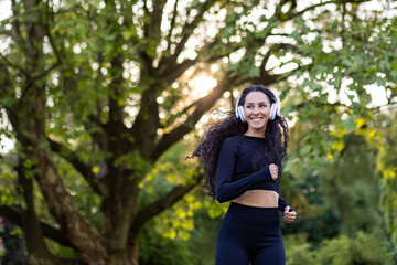 Young beautiful hispanic woman running with headphones, woman jogging in the morning in the park, using headphones to listen to music, audio podcasts, and online radio.