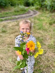 Beautiful little boy holding daisy flower in field outdoor. Bouquet close up. Vertical photo