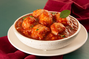 Delicious Gnocchi with Red Sauce and Basil served in a White textured Handmade Ceramic Bowl in a green background decorated with red fabric crossing the frame in front view