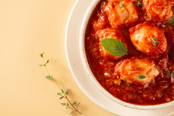 Delicious Gnocchi with Red Sauce and Basil served in a White textured Handmade Ceramic Bowl in a beige clean background with thyme decoration in cropped top view