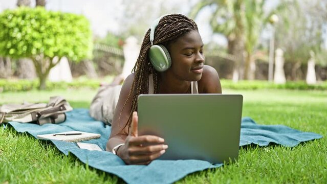 African american woman student using laptop and headphones lying on floor at campus university