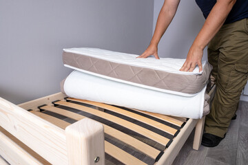 A roll of a new mattress in a man's hands before making his bed on a new wooden bed