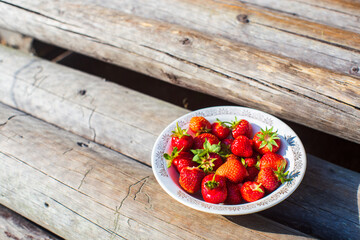 Close-up strawberry crop lying in a plate on rural wooden steps. The concept of healthy food, vitamins, agriculture, market, strawberry sale