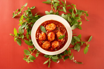 Delicious Gnocchi with Red Sauce and Basil served in a White textured Handmade Ceramic Bowl in a red and basil background in top view