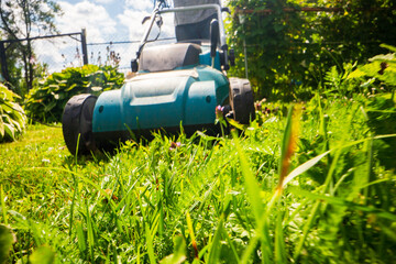 Lawn mover on green grass in modern garden or backyard. Machine for cutting lawns. Gardening care tools and equipment. Process of lawn trimming