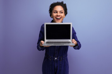 young pretty brunette latin woman with afro ponytail dressed in denim clothes holding a laptop...