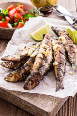Traditional Italian barbecue sardines with tomato salad and lemon slices served as close-up on an design stone board