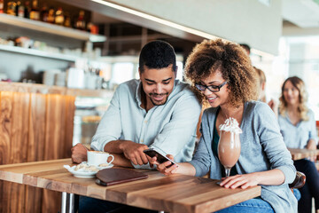 Young couple using a smart phone in a cafe while enjoying a cup of coffee