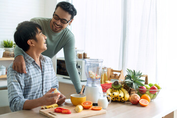 LGBTQ couple making various fruit  healthy smoothies for breakfast in their kitchen at home, looking and smiling at each other, healthy food concept