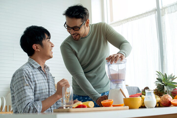 LGBTQ couple making various fruit healthy smoothies for breakfast in their kitchen at home, pouring smoothie to glass, healthy food concept