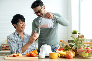 LGBTQ couple making various fruit healthy smoothies for breakfast in their kitchen at home, pouring smoothie to glass, healthy food concept