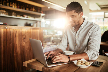 Young man using a laptop while having coffee at a cafe in the city