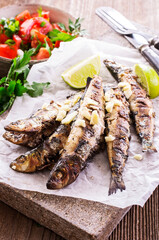 Traditional Italian barbecue sardines with tomato salad and lemon slices served as close-up on an design stone board