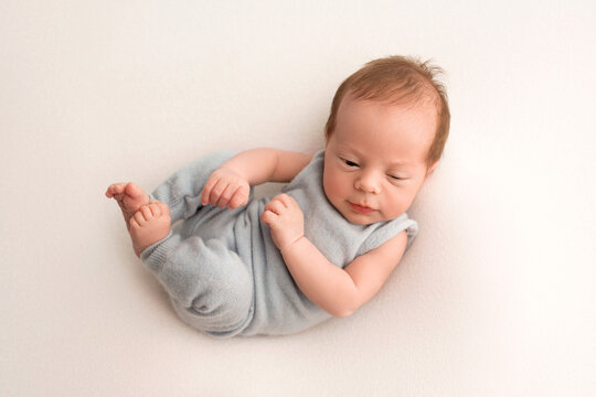 A cute newborn baby boy lies in a blue overalls in the first days of life. On a white background. Professional macro photography. Portrait.
