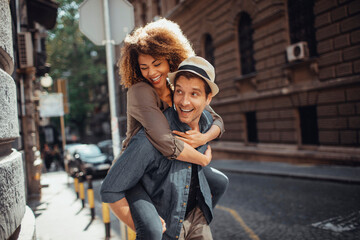 Young man carrying his girlfriend on a city street while they are traveling on their vacation