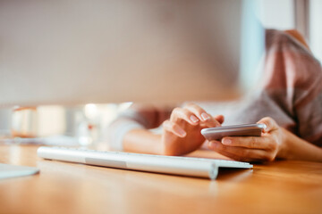 Fototapeta premium Young woman using a smart phone at home while working on her computer