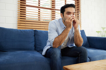 young man having a cold, using tissue paper and blowing his nose on sofa