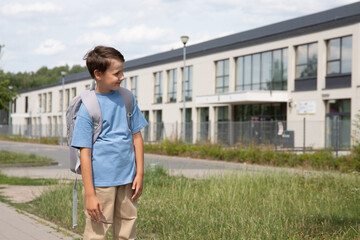 8-year-old boy in a blue T-shirt and light pants is standing near school. concept of education, back to school, school year, finished school