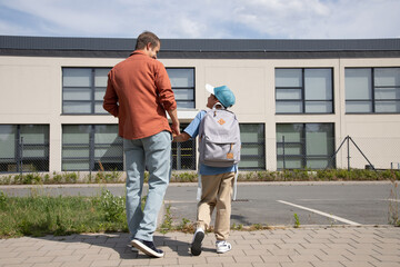 dad is holding his son's hand. father and son go to school. Parental care, return to school, education. rear view. the first day of school.