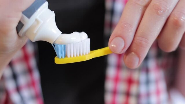 Squeezing out toothpaste on a yellow toothbrush, close-up. Brush your teeth. Health care, dental hygiene. A woman in the bathroom is squeezing white toothpaste out of a tube