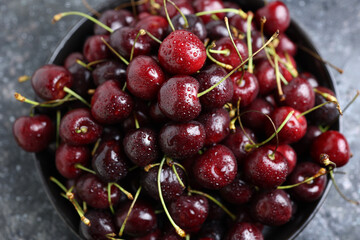 red cherry berries with water drops in a dark ceramic bowl on a dark background.