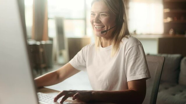 Excited emotional mature blond woman gamer sitting at desk and playing in video games on computer at home Happy player female take part in online competition and talking to players online indoors