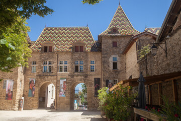 Fototapeta na wymiar Ensemble architectural recouvert de tuiles vernissées et des arches accédant à une place du village de Saint-Antoine l'abbaye (Isère)
