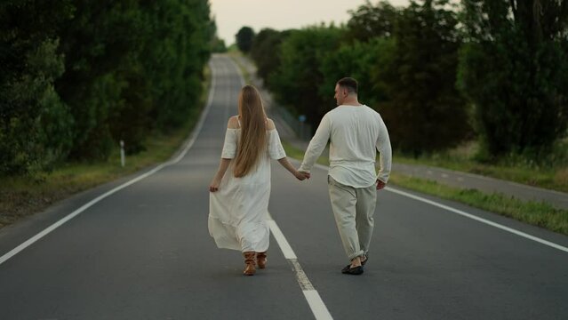 A woman and a man walk along the road holding hands