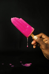 Pink ice cream on a stick in hand on a black background.