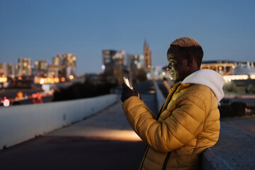 Young African American man using cell phone app in the modern city at night 