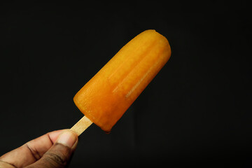 Orange ice cream on a stick in hand on a black background.