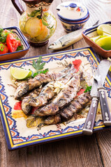 Fototapeta na wymiar Traditional portuguese barbecue sardines with tomato salad and lemon slices served as close-up on a classic design board
