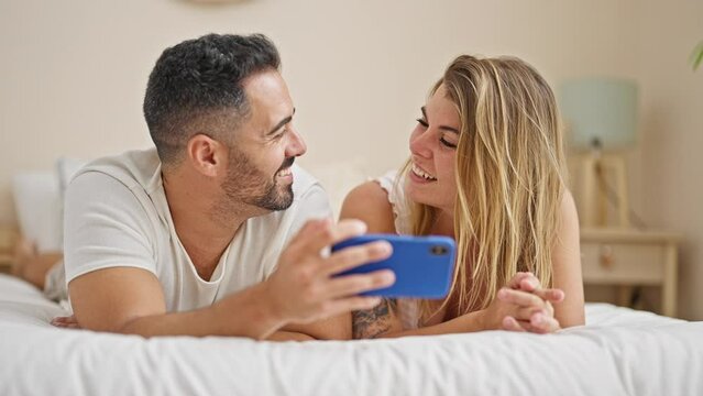 Man and woman couple lying on bed using smartphone speaking at bedroom