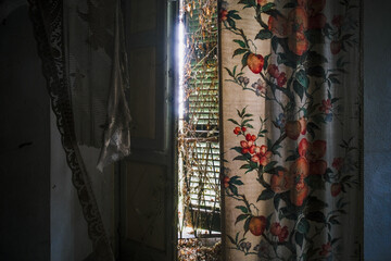 window with ajar shutters and floral curtain in an abandoned house