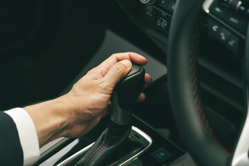 Hand of Business man with watch holding driver shifting the gear stick. Driving car concept. Safe...