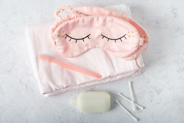 Silk pink eye mask lying on the white bedding in the morning, top view. Sleep well concept.