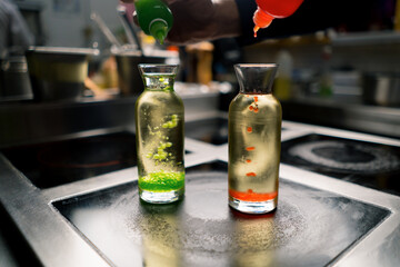 a chef in a professional kitchen experiments by adding multi-colored molecular caviar grains to a...