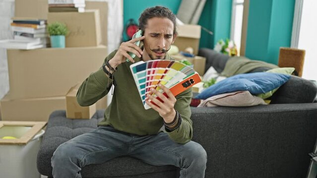 Young hispanic man talking on smartphone holding color test at new home
