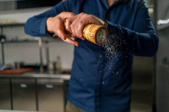 close-up of a chef holding a pepper and salt grinder in his hands grains of spices fall in the air