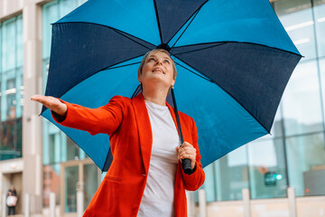 a woman in a red jacket with coffee under an umbrella walking around a modern city