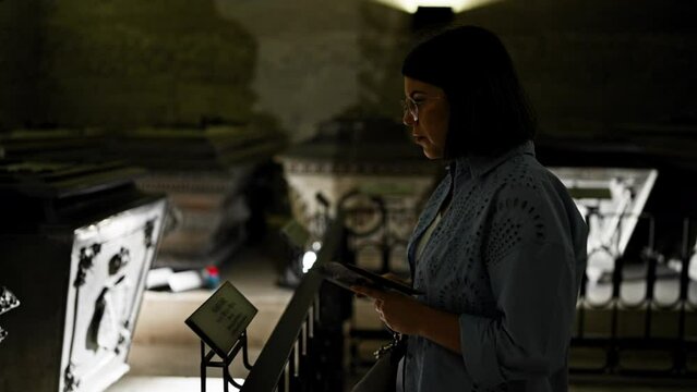 Young beautiful hispanic woman visiting crypt reading brochure at Imperial Crypt in Vienna