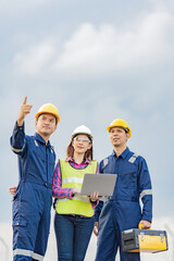 A team of 3 Asian male and female engineers with a mechanic manager point and look at the destination Talk about the energy industry holding via tablet tool box Wear a helmet and mechanic's uniform.