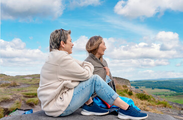 two women travellers in a white jacket traveling reaching destination and resting on the top of rock in Peak District. Local tourism lifestyle concept