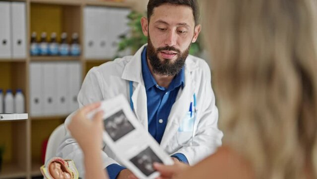 Young hispanic man gynecologist showing ultrasound to patient at the clinic