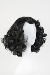 Fototapeta premium Natural looking black wig on white mannequin head. Medium length curly wavy hair on the metal wig holder isolated on white background, side view