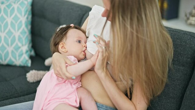 Mother and daughter sitting on sofa breastfeeding baby at home