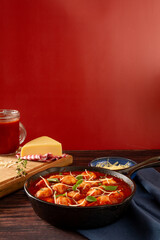 Delicious Gnocchi with Red tomato Sauce and Basil served in a black skillet pan in a red background in front view