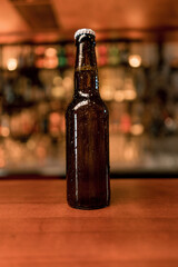 Close up of a closed bottle of beer with labels standing on a bar counter in a club bar 