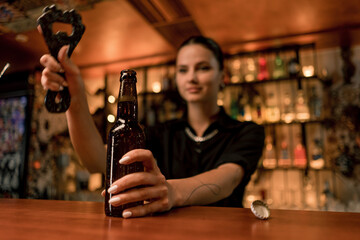 Close up of a female bartender opening a closed glass bottle of beer on the bar in a club bar