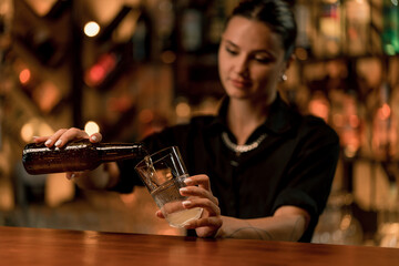 Close up of a female bartender pouring beer from a bottle into a glass on the bar in a club bar